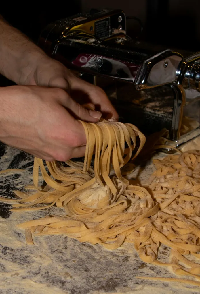 Hands gathering freshly cut tagliatelle on a pasta machine
