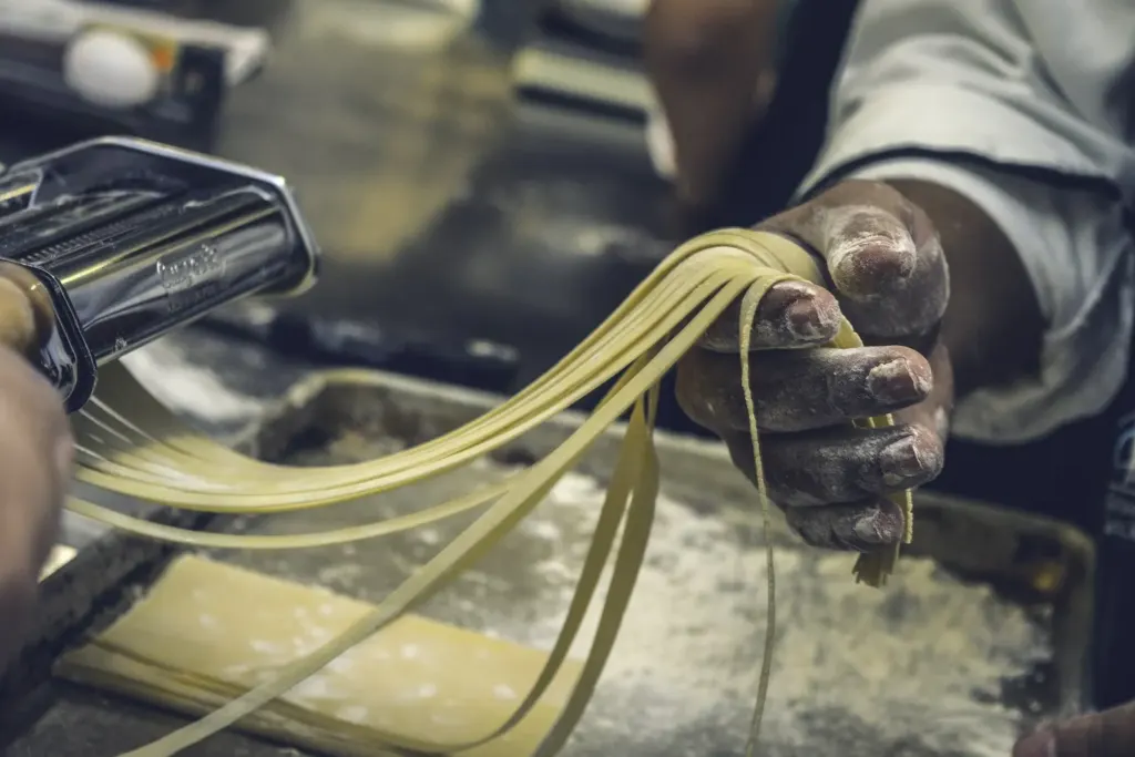 A cook rolling fresh pasta dough through a pasta machine
