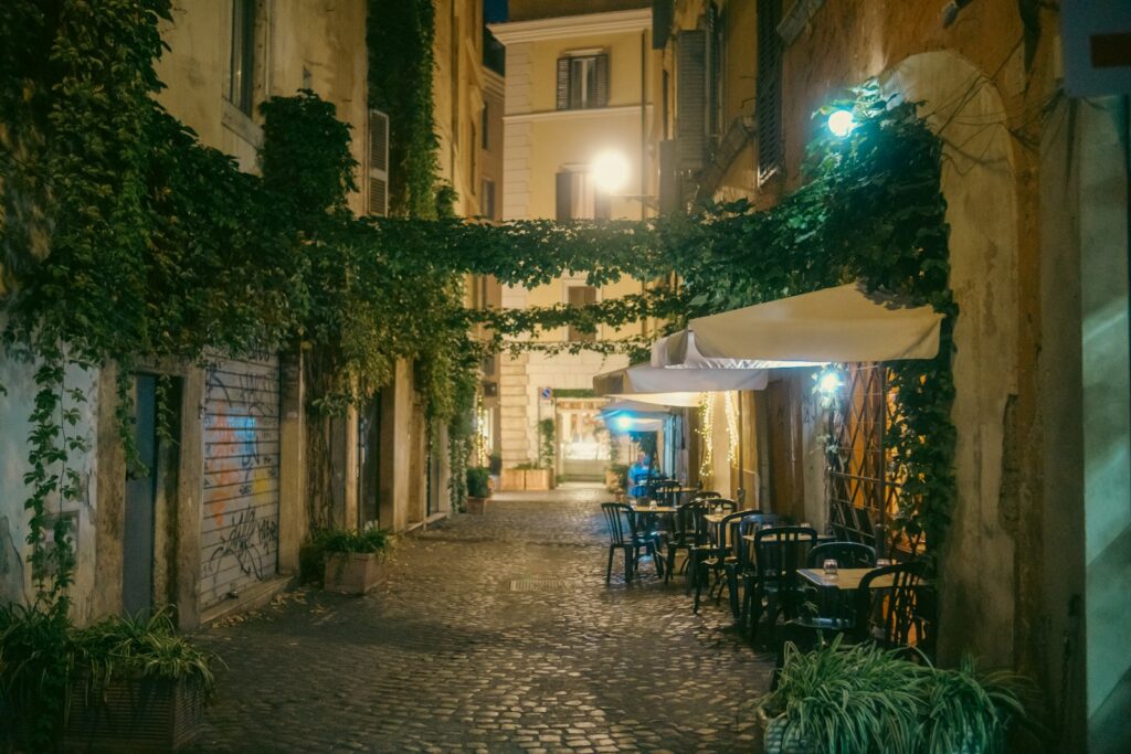 Ivy-covered cobbled lane with restaurant tables in Trastevere at night