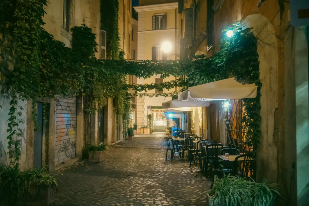 Ivy-covered cobbled lane with restaurant tables in Trastevere at night