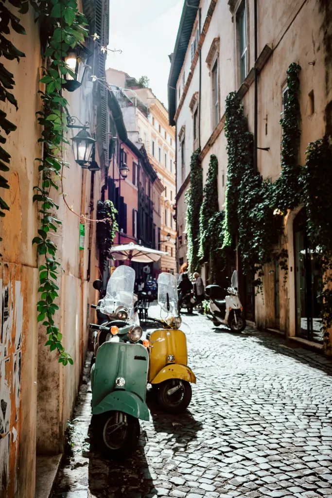 Two vintage Vespa scooters parked on an ivy-lined cobbled lane